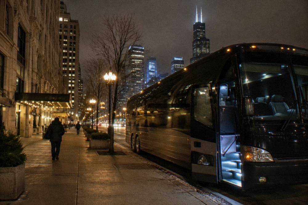 A coach bus parked on a Chicago street at night with city lights in the background