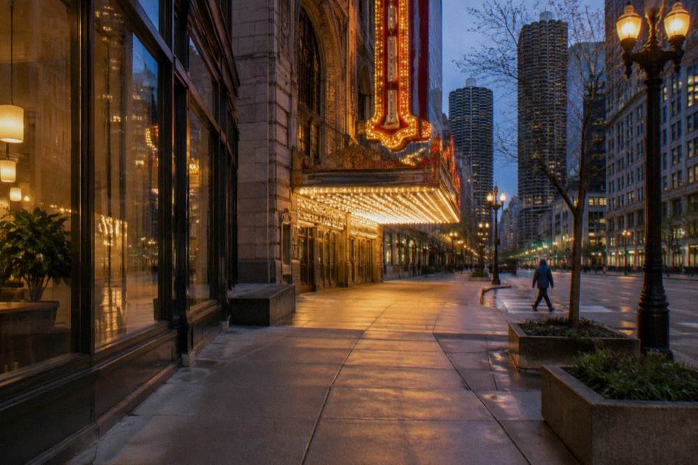 A wide downtown Chicago sidewalk at night with crosswalk ramps and glowing storefronts
