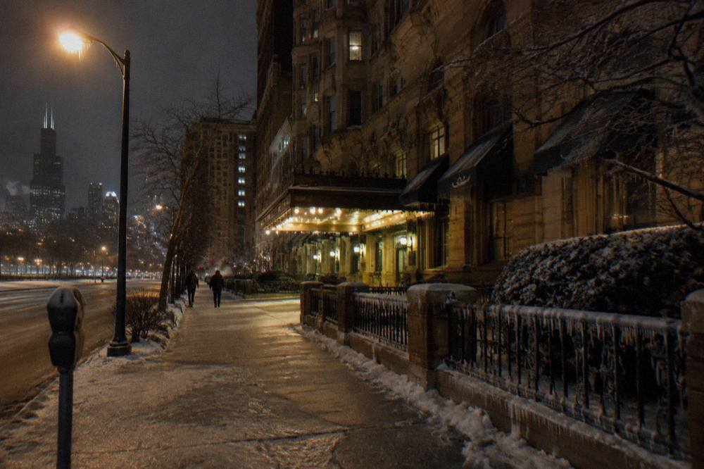 Frost-covered Chicago sidewalk at night lit by a single streetlamp between old brick buildings