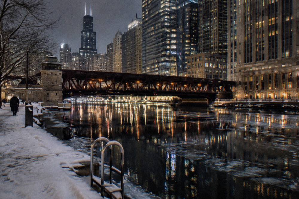Snow-dusted Chicago riverfront at night with lit bridges and downtown towers behind