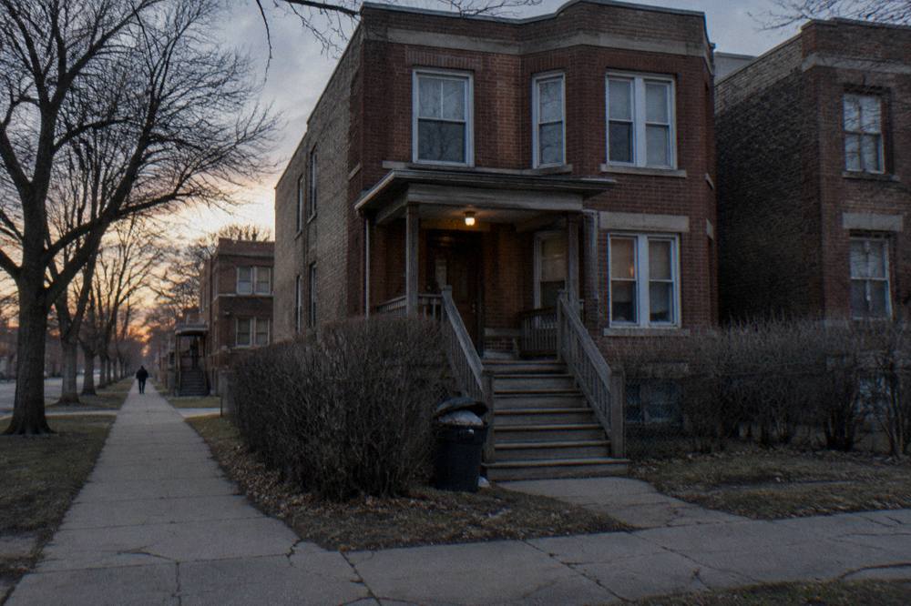 A brick two-flat house on a quiet Chicago street seen from the sidewalk in late afternoon light