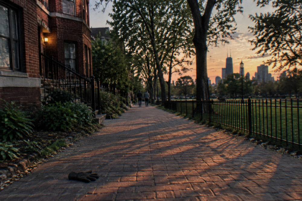 Narrow Lincoln Park sidewalk at dusk with tree shadows across old brick buildings