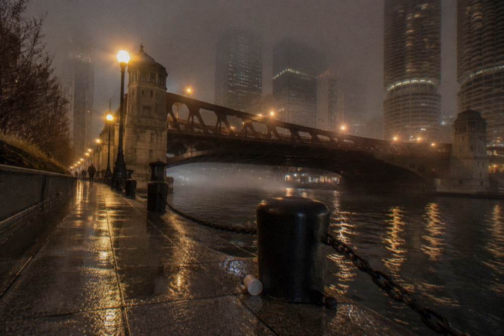 Foggy Chicago riverfront street at night with bridge lights reflecting on wet pavement