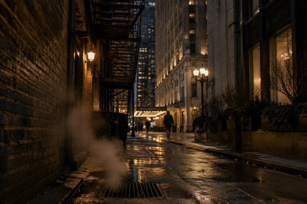 A lantern-lit brick alley in Chicago at night with fire escapes overhead