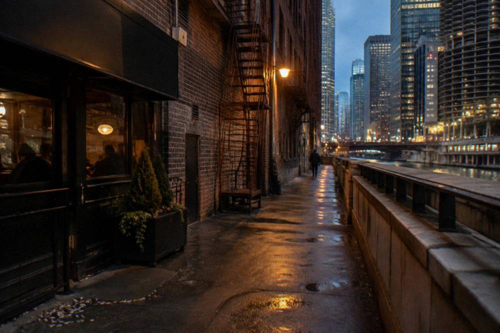 A dark Chicago alley with brick walls and a single lit lamp in the evening