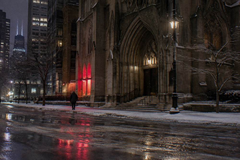 City street at night with wet pavement reflecting vintage neon signs along a brick facade