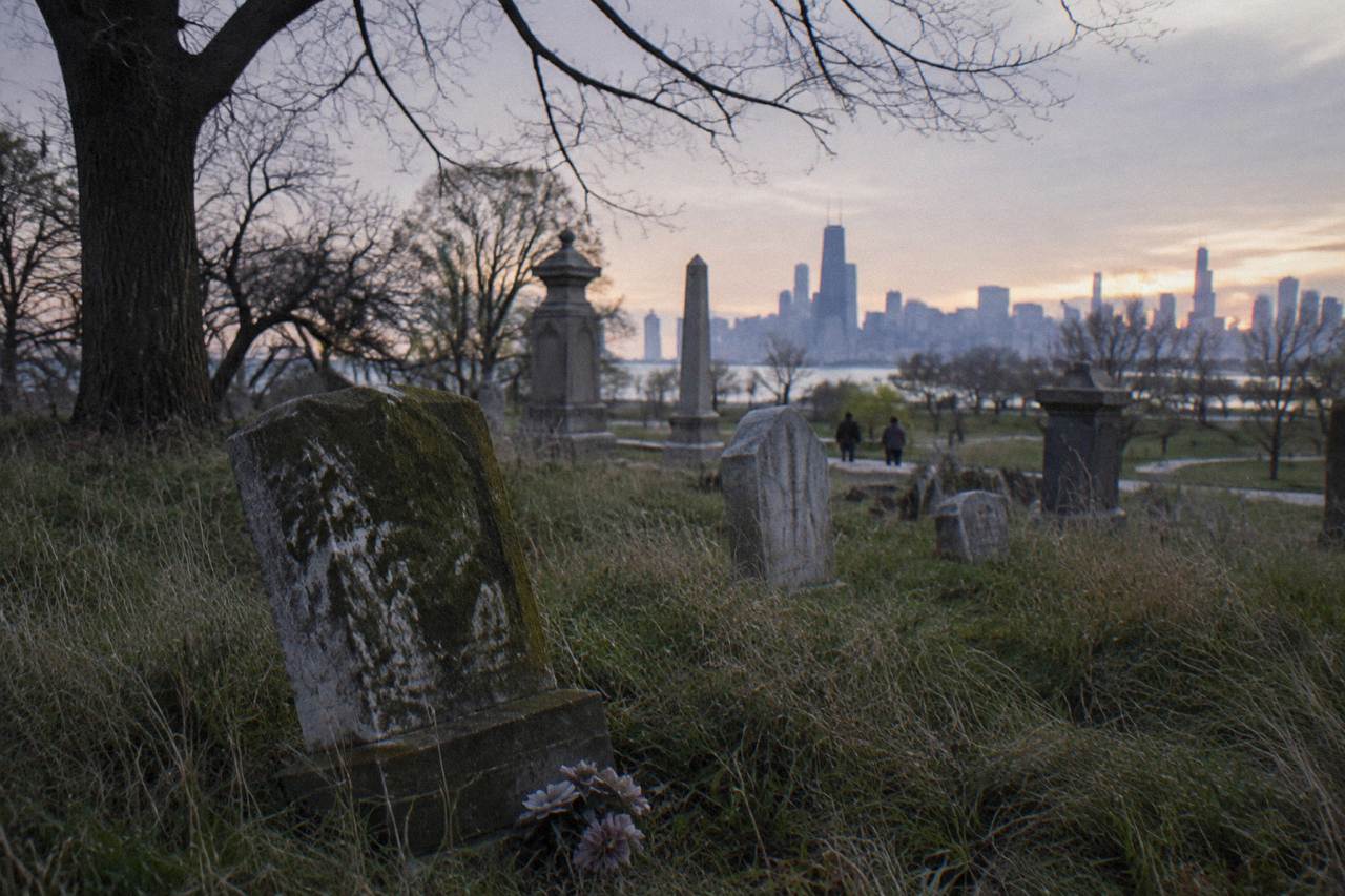 Weathered gravestones in an old Chicago cemetery at dusk with bare trees