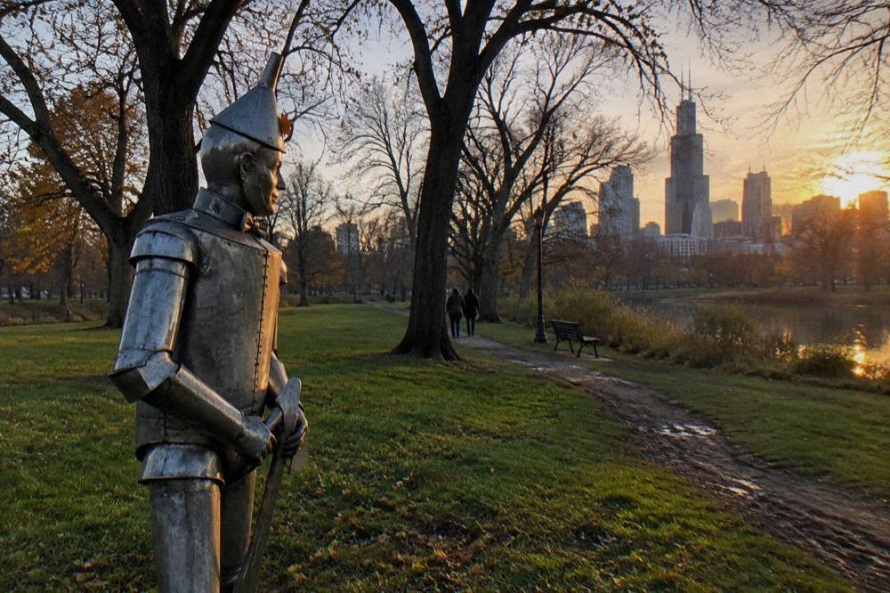 The Tin Man statue standing in Oz Park at golden hour with trees behind it