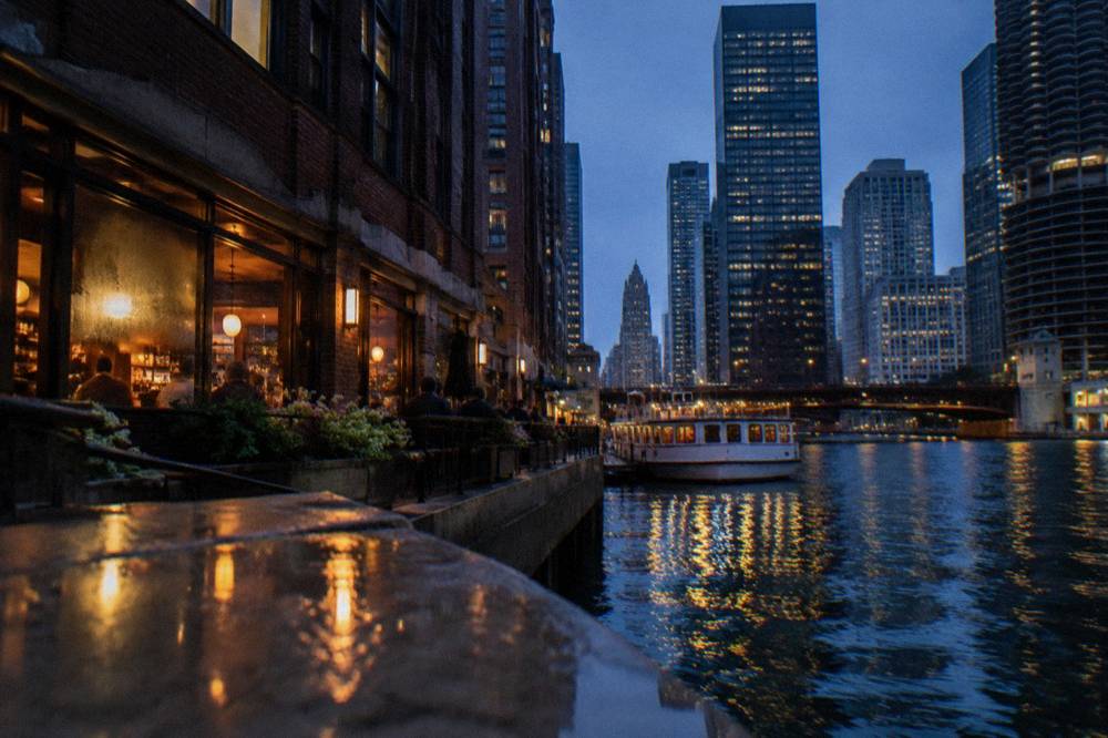 Wacker Drive sidewalk along the Chicago River at dusk with lit towers above