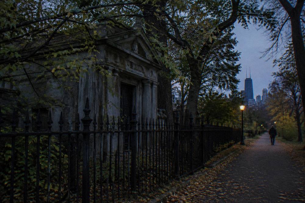Dark tree-lined path beside a Chicago cemetery fence at twilight
