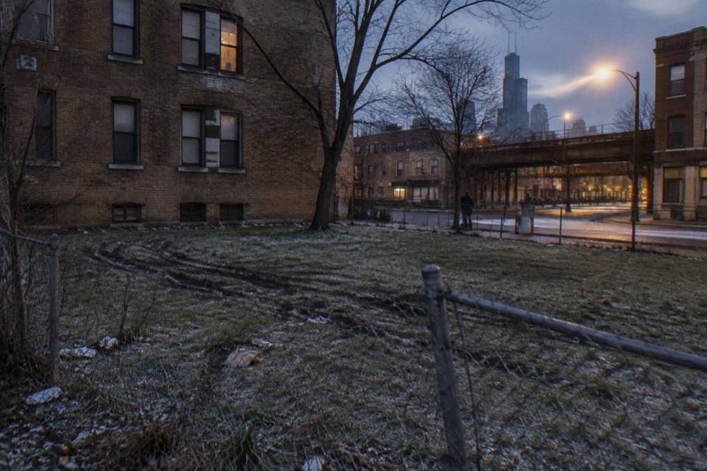 Fenced grassy lot beside a brick apartment building on a quiet Chicago street