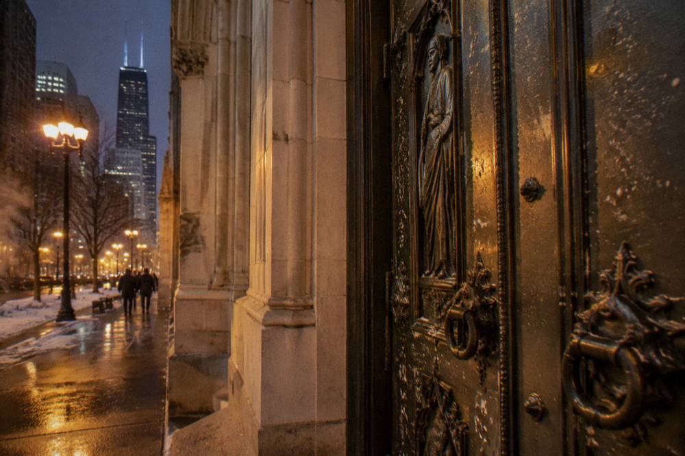 Bronze church doors with visible marks under evening streetlight