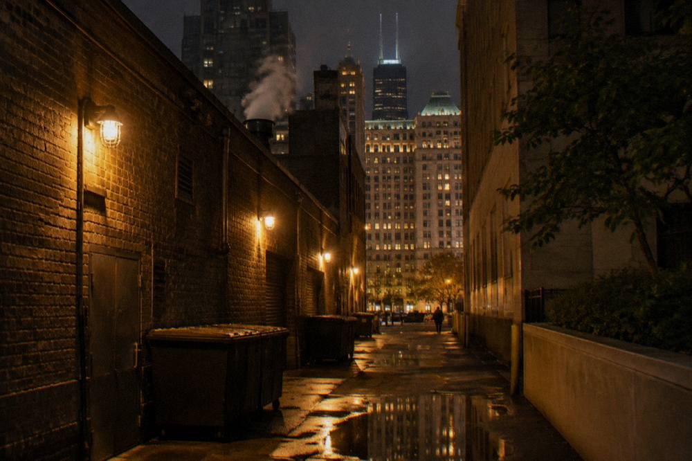 A dark alley between tall brick buildings in the Chicago Loop at night