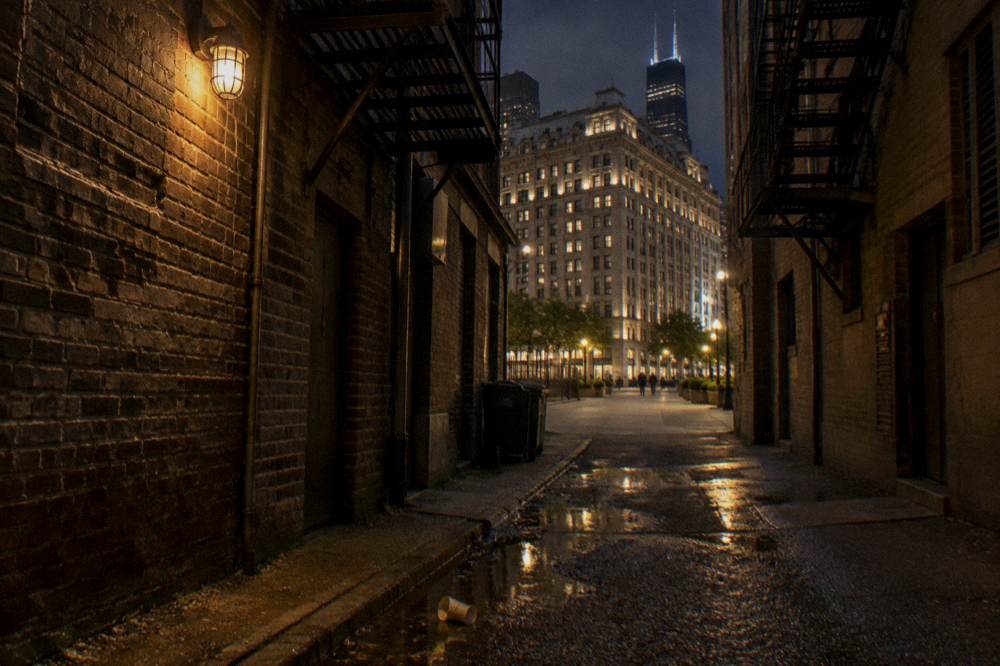 Narrow Chicago alley at night lit by a single lamp between old brick walls