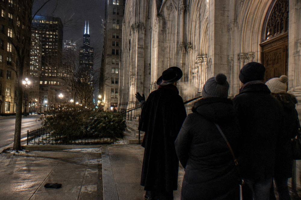 Tour guide addressing a small group on a downtown Chicago sidewalk at night