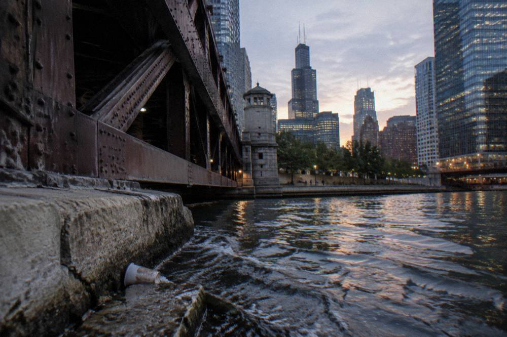 A plaque on the south bank of the Chicago River at dusk with the skyline behind it