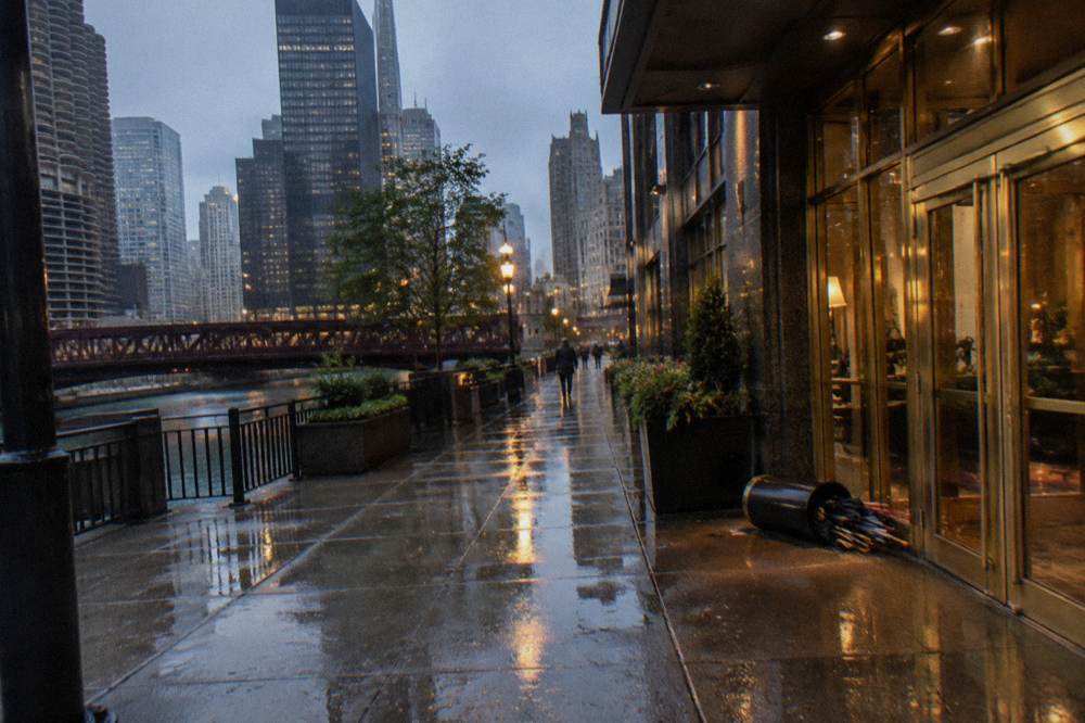Rain-specked pavement outside a lit Chicago hotel entrance in the evening