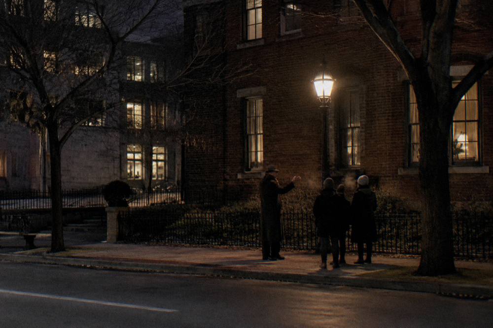 A guide in costume telling stories to a small group outside a Lincoln Park tavern at night