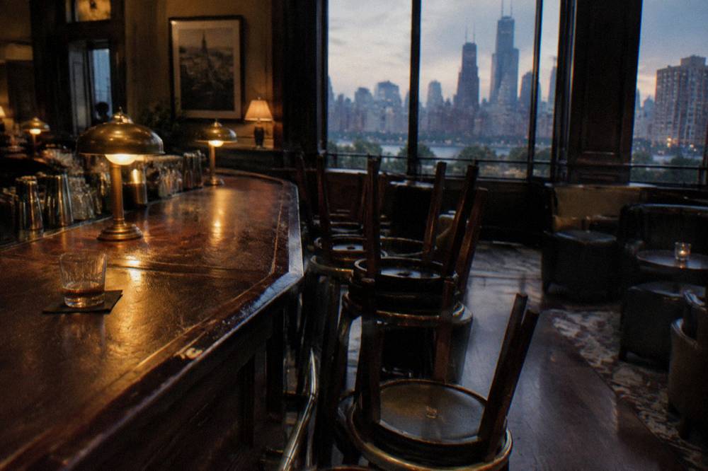 A dim bar interior with polished wood counter and empty stools before opening