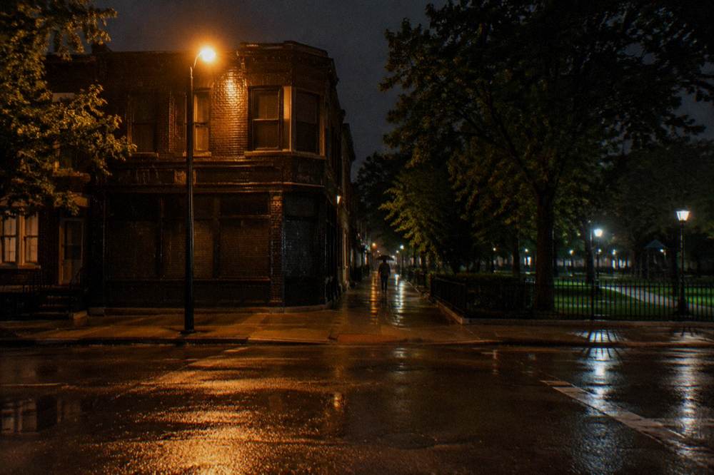 Nighttime sidewalk outside a closed tavern with the lights of Lincoln Park streets beyond