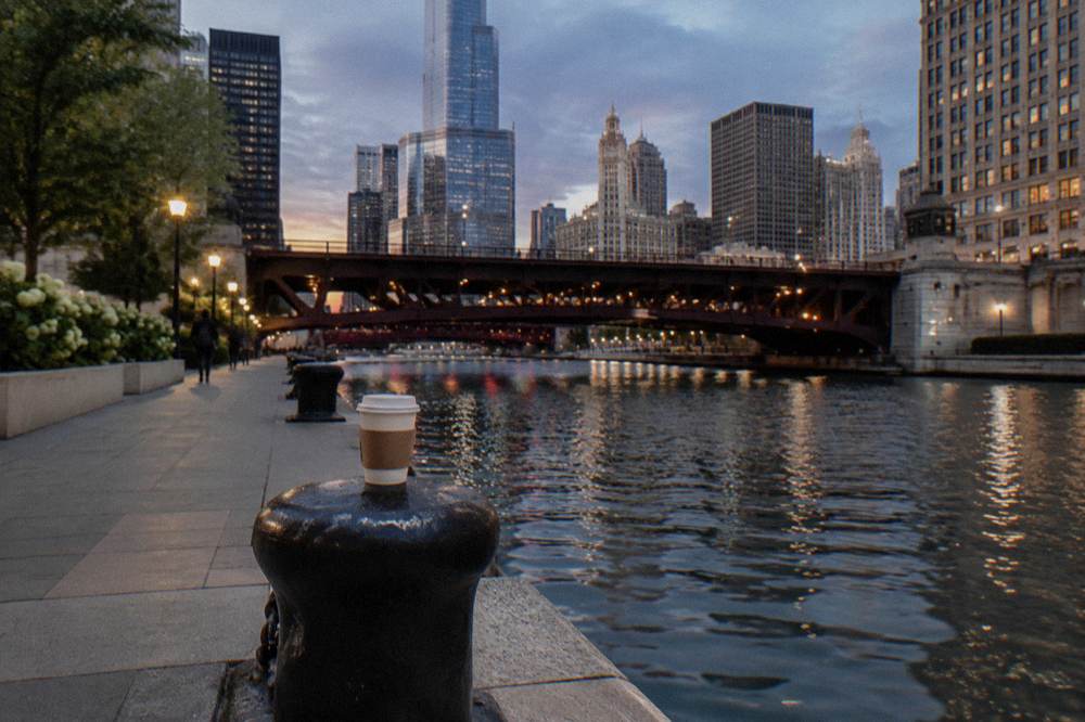 A wide sidewalk along the Chicago River at twilight with bridge lights