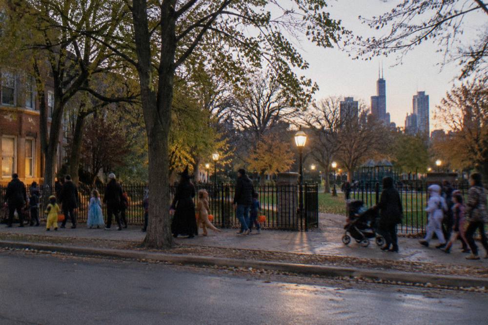 Crowded sidewalk at dusk in Lincoln Park with fall trees and lit storefronts