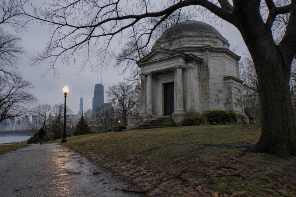 Dark tree canopy and a lamplit path through a Chicago park at dusk