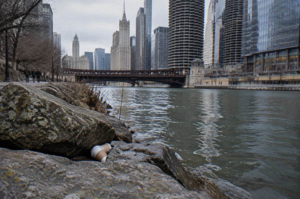 Granite historical plaque on the Chicago River bank with office towers rising behind it
