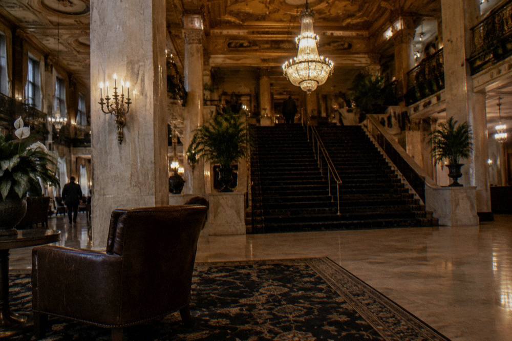 Grand historic hotel lobby with marble columns, chandeliers and a dark carpeted staircase