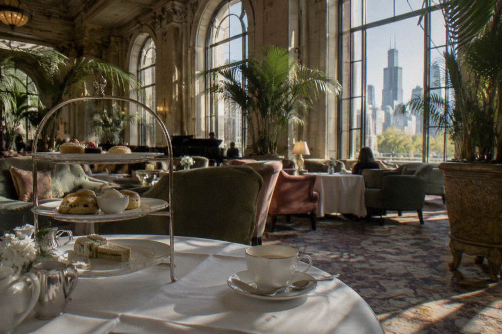 Palm Court style hotel lounge with tall arched windows, potted palms and tiers of afternoon tea seating
