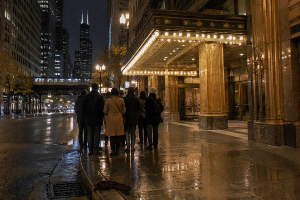 Guided walking tour group gathered on a downtown Chicago sidewalk at night with a lit hotel entrance behind them
