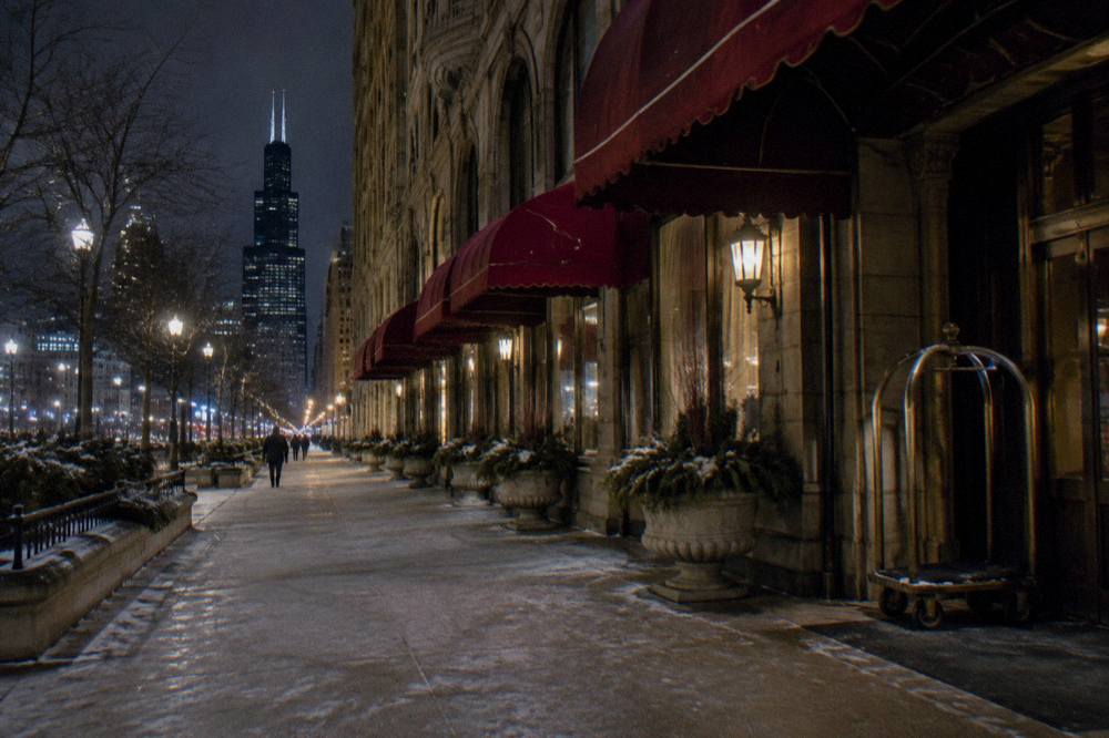 A historic Chicago hotel facade lit at night with an empty sidewalk below