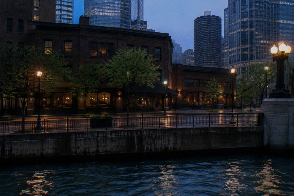 A Chicago city block at dusk with brick buildings and an empty sidewalk under street lights