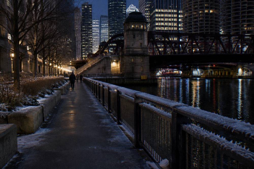 A dark Chicago riverfront walkway with bridge towers silhouetted against city lights