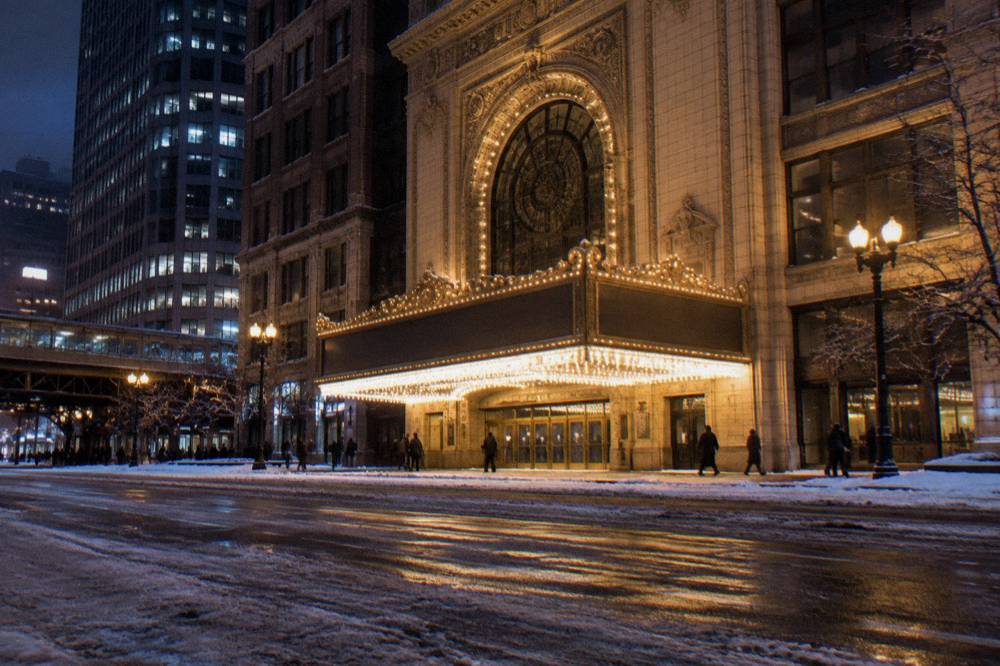 A wide Chicago avenue at night with lit theater marquees and light traffic