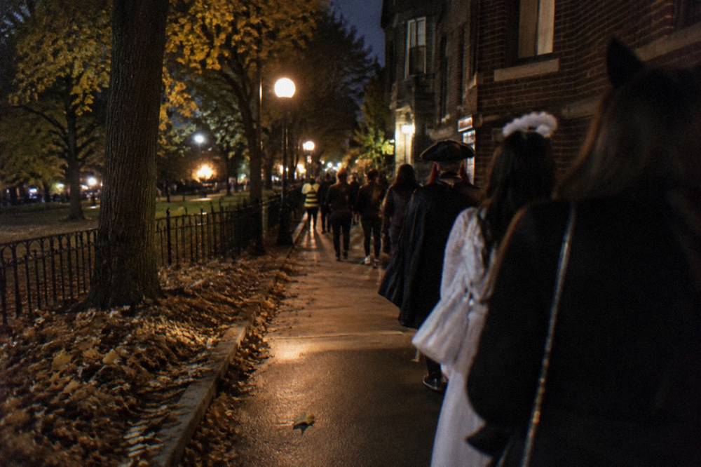 A crowded Lincoln Park sidewalk at night in autumn with fallen leaves and warm street lamps.