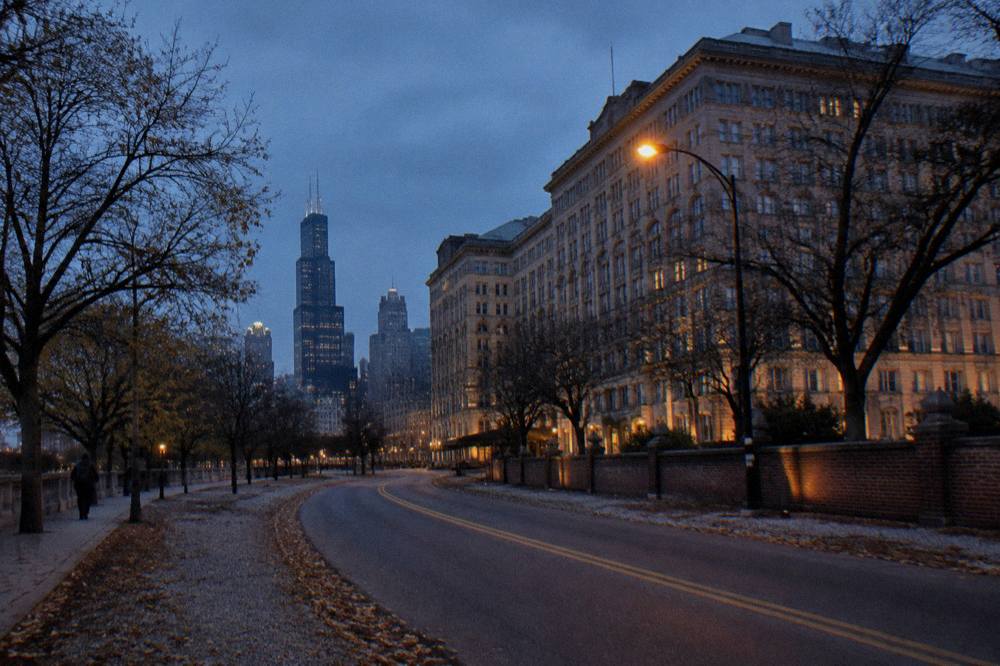 An empty two-lane road at dusk with bare trees on both sides