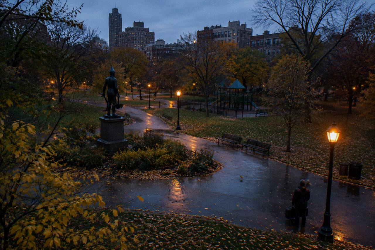 Oz Park at blue dusk with the tin statue silhouetted against amber streetlamps and fallen leaves on the path